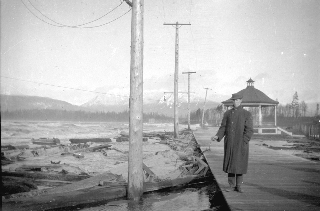 Man standing on wooden sidewalk at shore of Kitsilano Beach during a storm, 191?. Image: Major Matthews